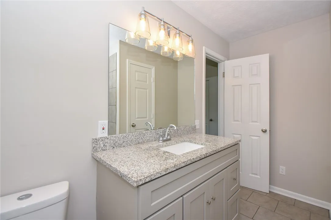 This bathroom features a sleek vanity with granite counters and a clean, tiled floor.