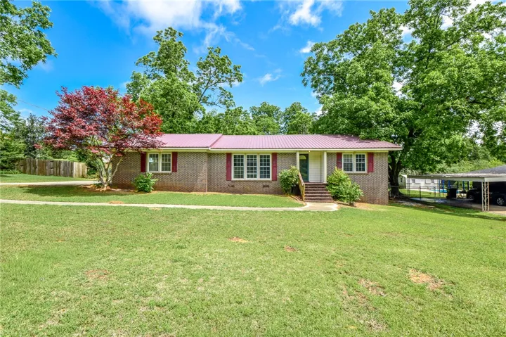 This charming home features a classic brick exterior and a vibrant red roof, nestled amidst lush greenery.