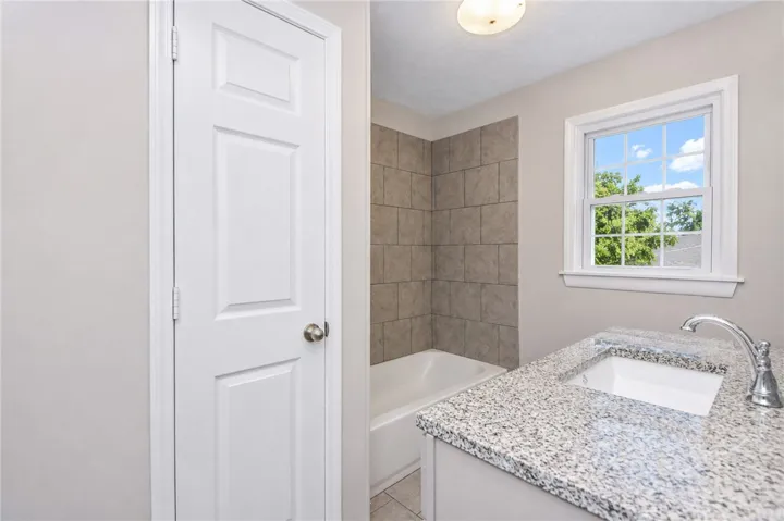 Bright and functional bathroom with granite counters and a tiled bath area.