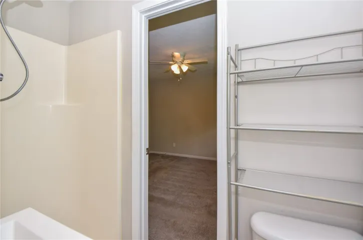 This bathroom features a functional shower and convenient open shelving, with a glimpse of an adjacent room.