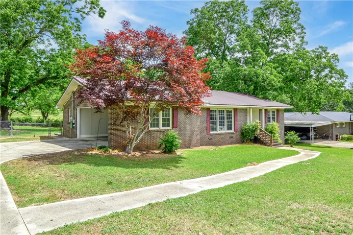 This classic brick residence features a lush lawn, concrete pathway, and mature trees, creating a welcoming facade.