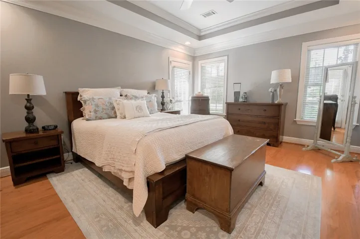 This primary bedroom features high ceilings, hardwood flooring, and ample natural light through large windows.