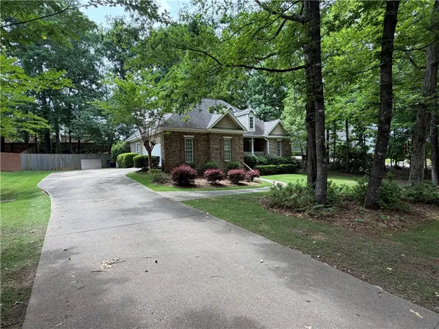 A graceful paved driveway leads to a classic brick residence nestled amidst lush, mature trees.