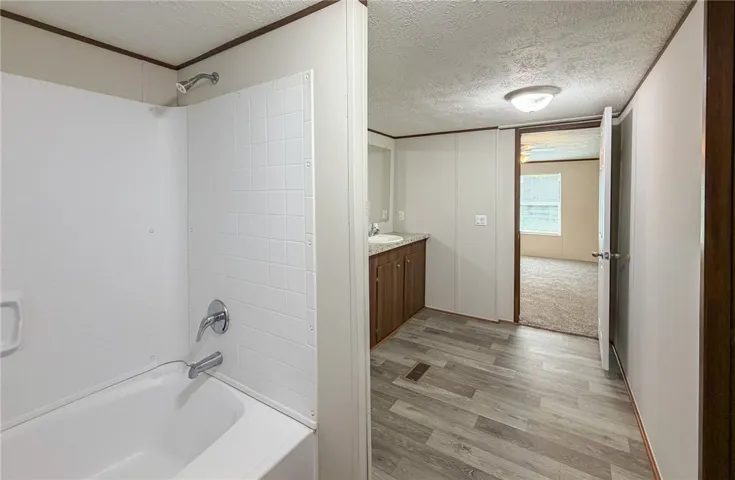 This bathroom features a bathtub and a vanity, with durable flooring leading to an adjacent room.