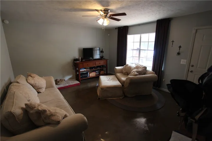 This inviting living area features a ceiling fan, ample natural light, and a clean, durable concrete floor.