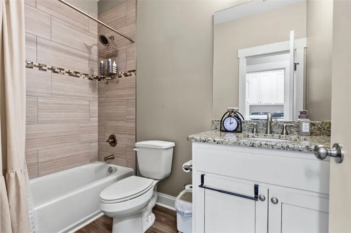 This clean bathroom showcases a pristine tub, toilet, and vanity with elegant granite counters.