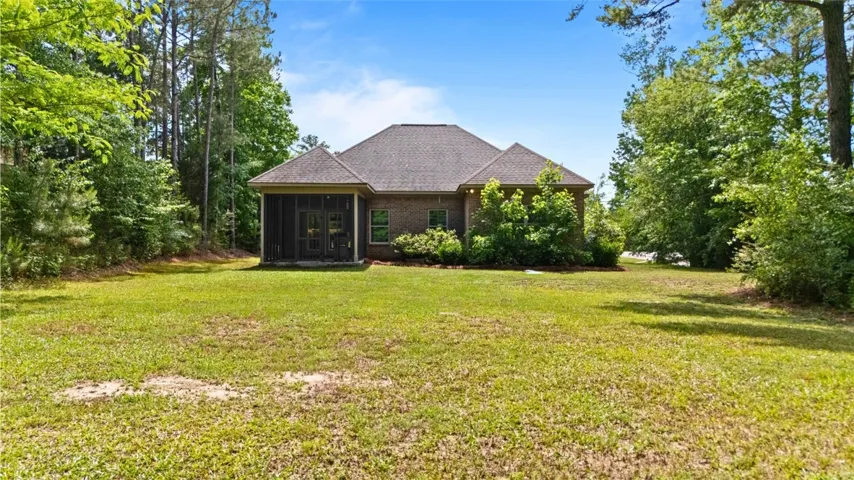 This residence features a large green yard, a screened porch, and a brick exterior, nestled among lush trees.