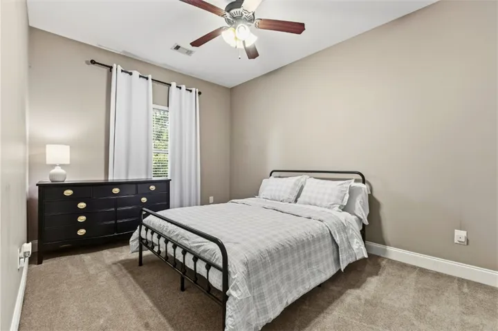 This cozy bedroom features a ceiling fan, plush carpet, and ample natural light.