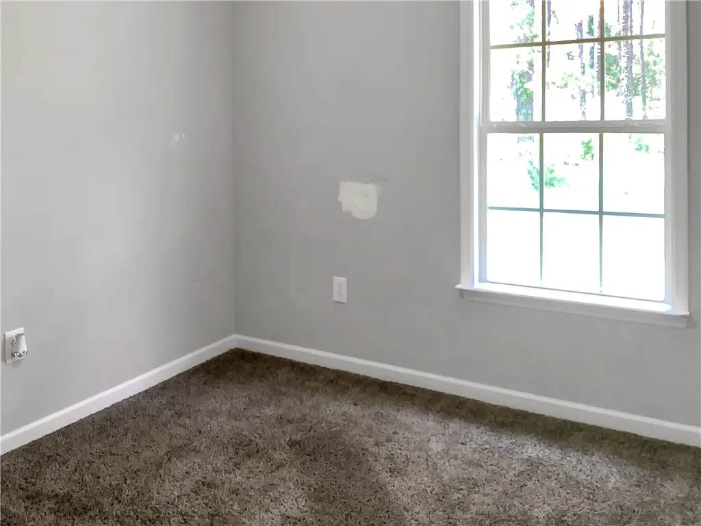 A well-lit room offers simple comfort with plush carpeting and a bright window.