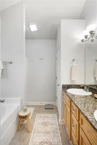 This bright bathroom offers a dual vanity with granite counters, tile flooring, and a relaxing soaking tub.