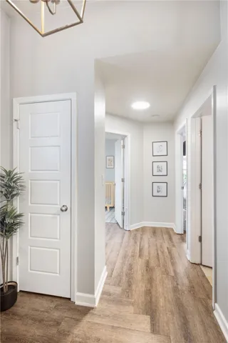 This bright hallway connects various rooms with warm flooring and a luminous ceiling light.