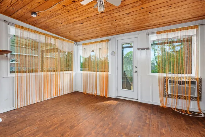 A well-lit enclosed porch features a wood plank ceiling and durable flooring, creating a cozy sunroom.