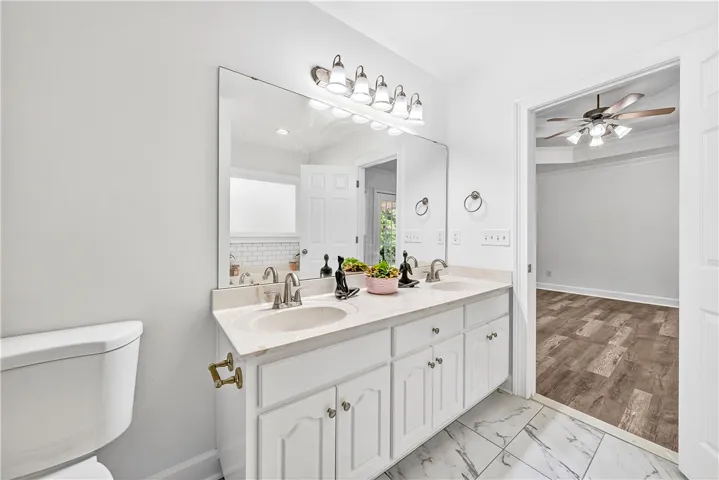 This primary bathroom offers a double vanity and a ceiling fan in the adjacent room for comfort.