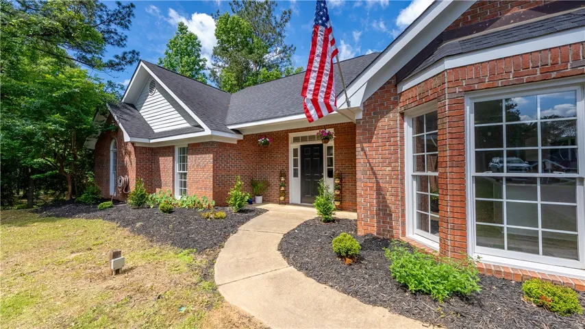A charming brick home features a welcoming entryway with a concrete pathway and well-maintained landscaping.