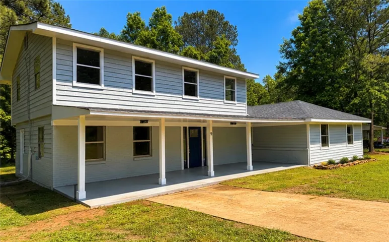 This two-story home features a welcoming covered porch, a well-maintained yard, and mature trees.