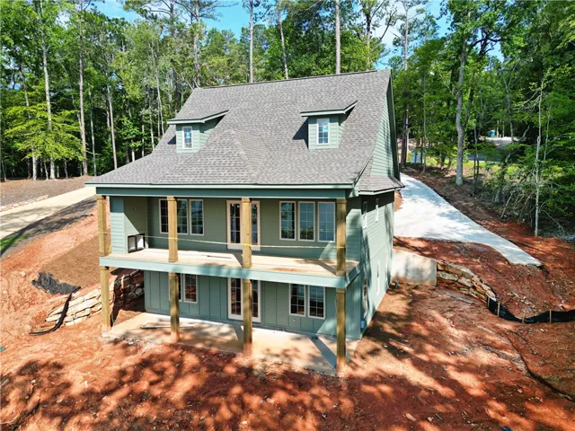 A newly constructed residence nestled into a wooded hillside, featuring dormer windows and a wrap-around porch.