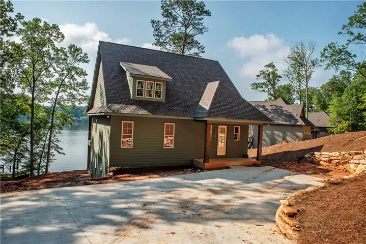 Green siding adorns this lakeside dwelling with a concrete driveway and rock landscaping.
