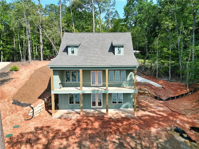 A newly constructed residence is nestled among mature trees on a sloped lot, featuring a broad deck and dual dormer windows.