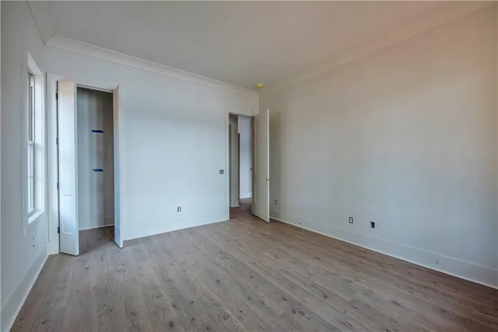 Natural light filters into this bedroom, featuring crown molding and light wood flooring.