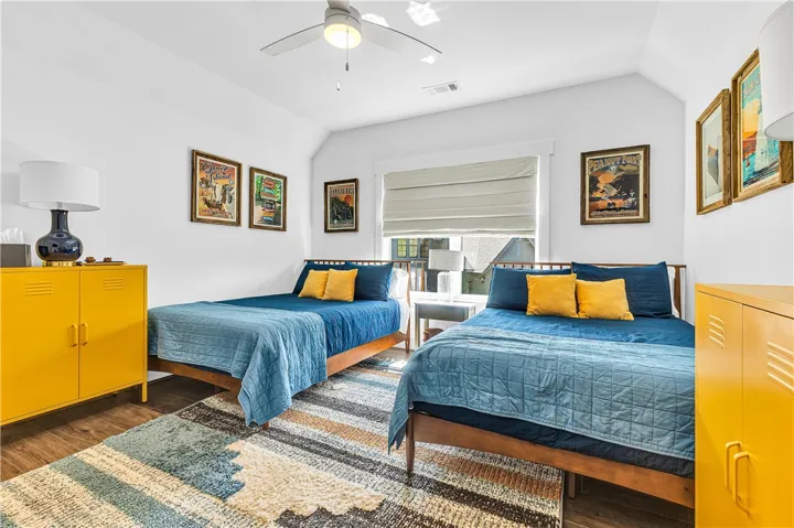 This bright bedroom features sloped ceilings, hardwood flooring, and abundant natural light through a large window.