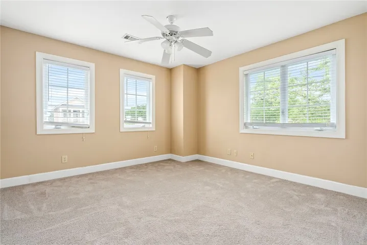 A well-lit bedroom with ample windows, soft carpet, and a convenient ceiling fan for comfort.