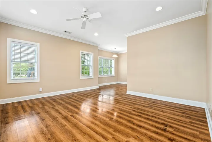 Natural light bathes this spacious room, featuring elegant crown molding and rich hardwood flooring.