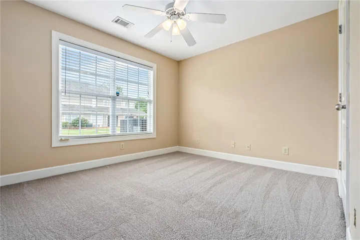 A well-lit bedroom features plush carpeting and a modern ceiling fan, inviting comfort and relaxation.