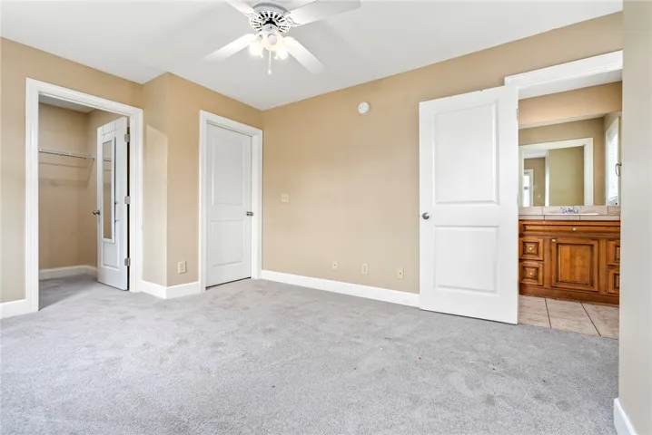 A comfortable bedroom with soft carpeting connects to a private bath, featuring a vanity and mirror.
