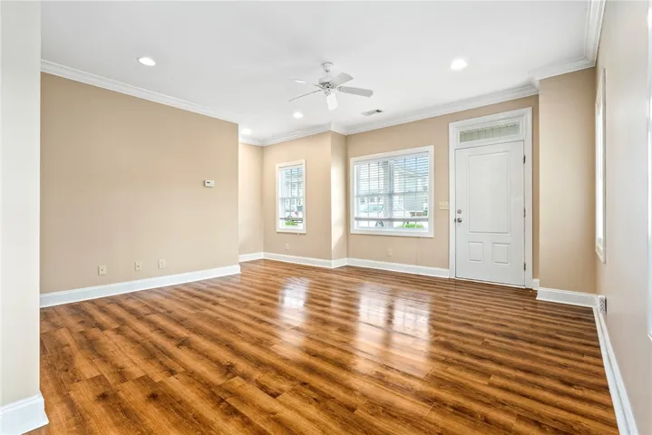 Natural light floods this inviting living space, highlighting its rich wood flooring and pristine crown molding.