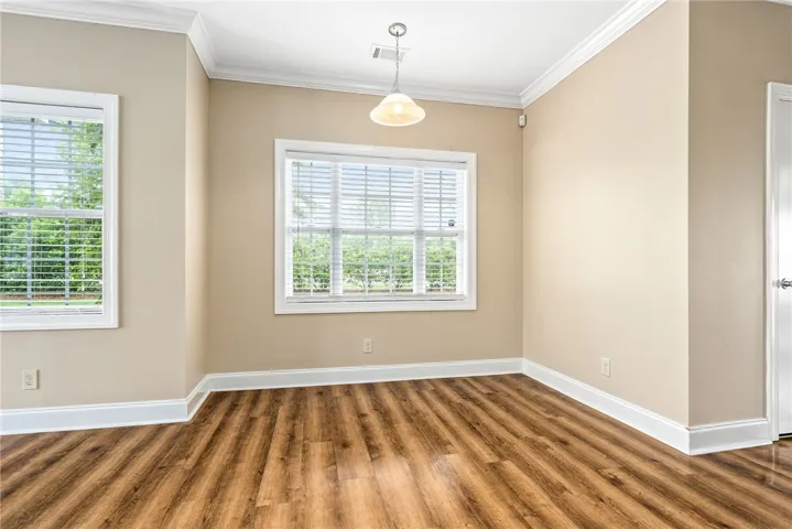 Luminous room featuring wide windows, warm wood-look flooring, and elegant crown molding.