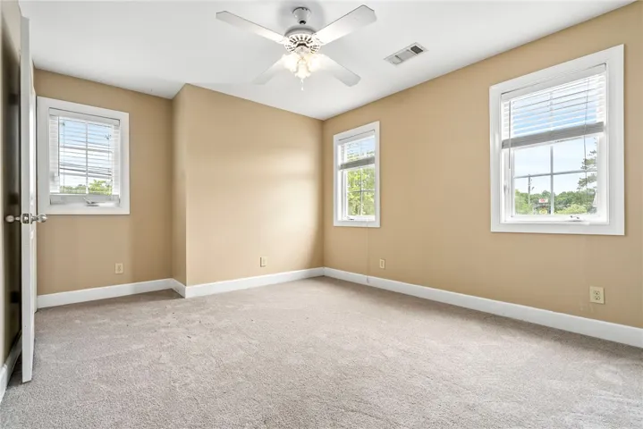 An inviting room features neutral walls, plush carpet, and ample natural light through three windows.