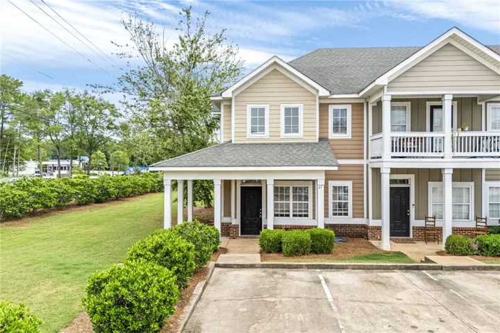 A charming townhouse with inviting curb appeal, featuring covered porches and an adjacent grassy lawn.
