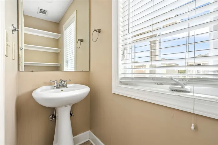A well-lit powder room offers a pedestal sink and convenient mirror.