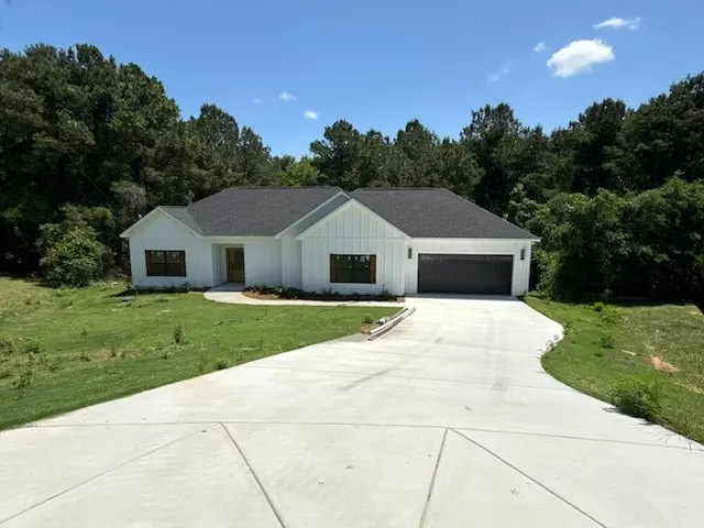This modern home offers a spacious concrete driveway and lush surrounding greenery.