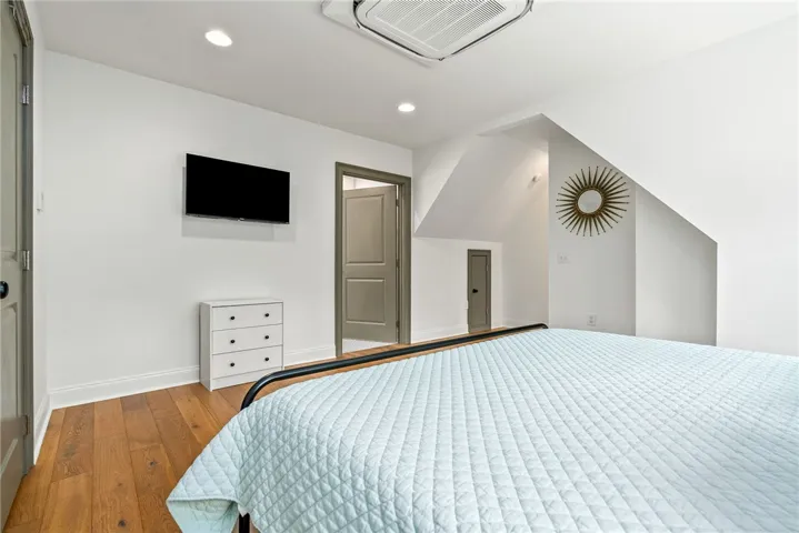 This cozy bedroom features warm hardwood flooring and recessed lighting, creating a comfortable and inviting atmosphere.