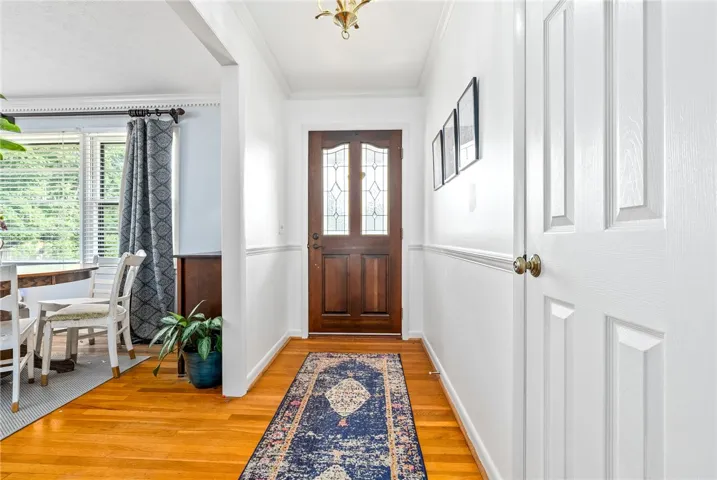 The bright entryway features red oak tongue and groove flooring, crown molding, and a classic wood door.