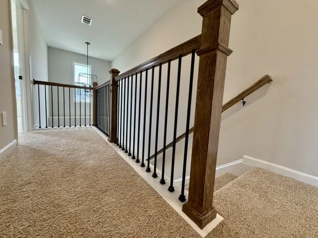 A well-lit landing features a contemporary chandelier and carpeted flooring, leading to a staircase with a wooden and wrought-iron railing.