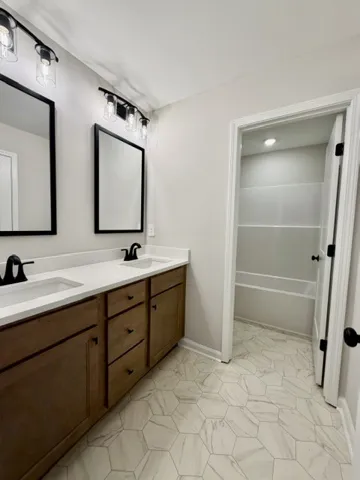 Double vanity sinks and hexagonal tile flooring elevate this pristine, naturally illuminated bathroom.