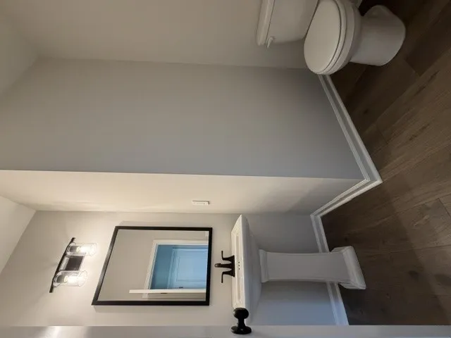 A well-lit bathroom with hardwood flooring, a contemporary mirror, and a pedestal sink.