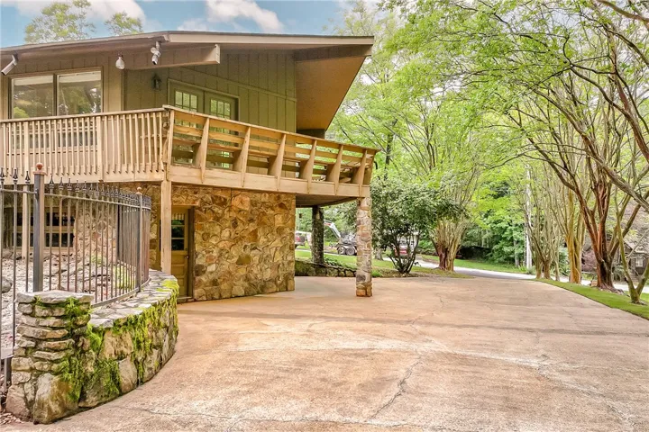 A stone-clad foundation supports a rustic home with an upper-level wooden balcony, offering a tranquil woodland retreat.