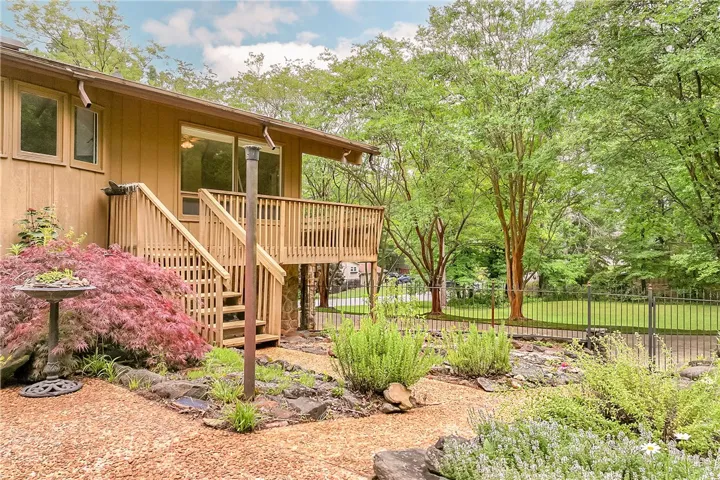 A spacious wooden deck extends from this house, surrounded by vibrant landscaping and mature trees.