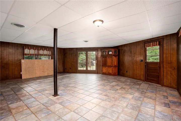A spacious lower level featuring durable tiled flooring and rustic wood paneling offers versatile living space.