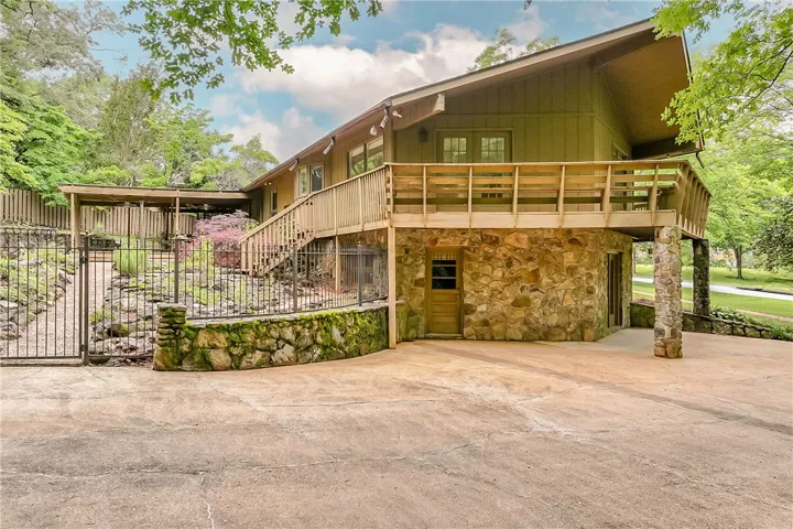 Discover a unique stone and wood exterior home, nestled amongst verdant trees with a spacious concrete driveway and charming wooden balcony.