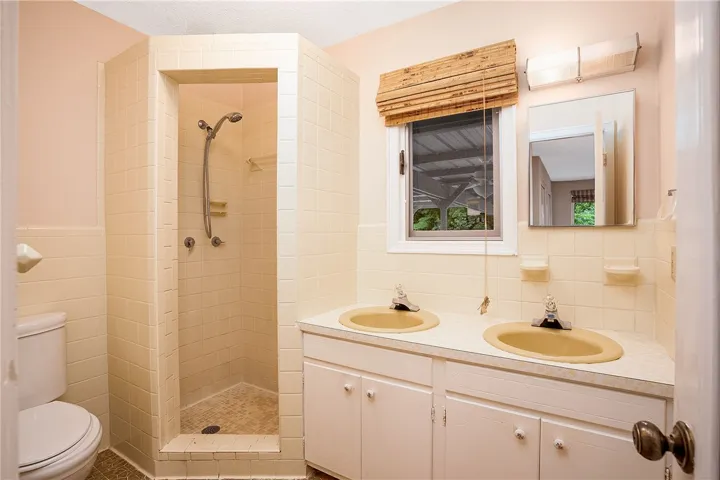 Well-lit bathroom with a standing shower and a dual-sink vanity, offering convenience and practical design.