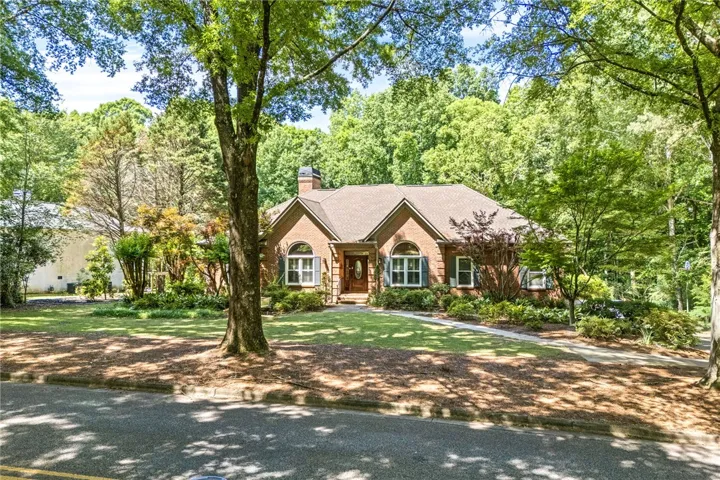 A well-kept front yard leads to a charming brick residence nestled among mature trees.