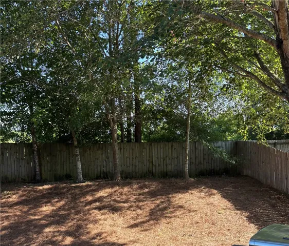 A well-maintained wooden fence provides privacy for this spacious yard, bordered by mature, leafy trees.