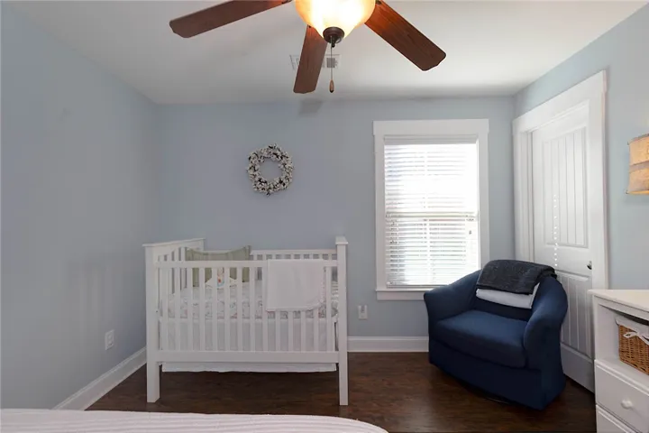 This cozy bedroom features warm wood flooring, a window with blinds, and a functional ceiling fan.