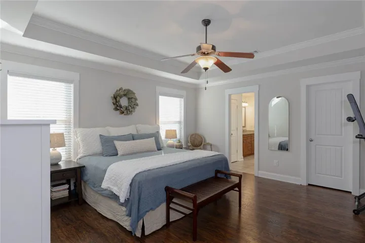 This primary bedroom offers warm hardwood floors, an inviting tray ceiling, and convenient access to the primary bathroom.