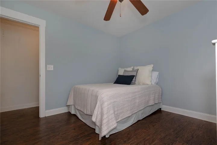 This cozy bedroom features rich wood flooring and a ceiling fan, offering comfort and style.