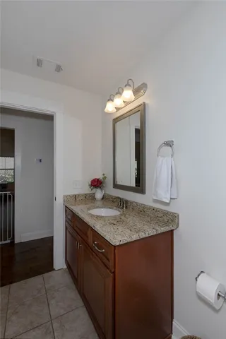 This bathroom offers a single vanity with granite counters and tiled flooring.